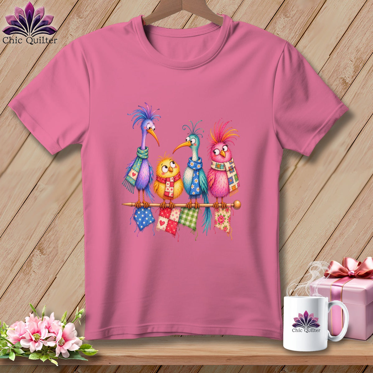 A pink t-shirt displays a graphic of four colorful cartoon birds wearing scarves on a rod.