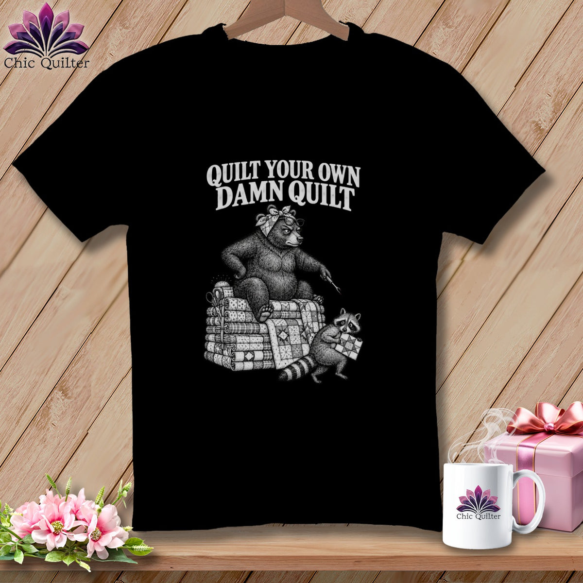 Black t-shirt featuring a vintage illustration of a bear and raccoon with the text Quilt Your Own Damn Quilt.