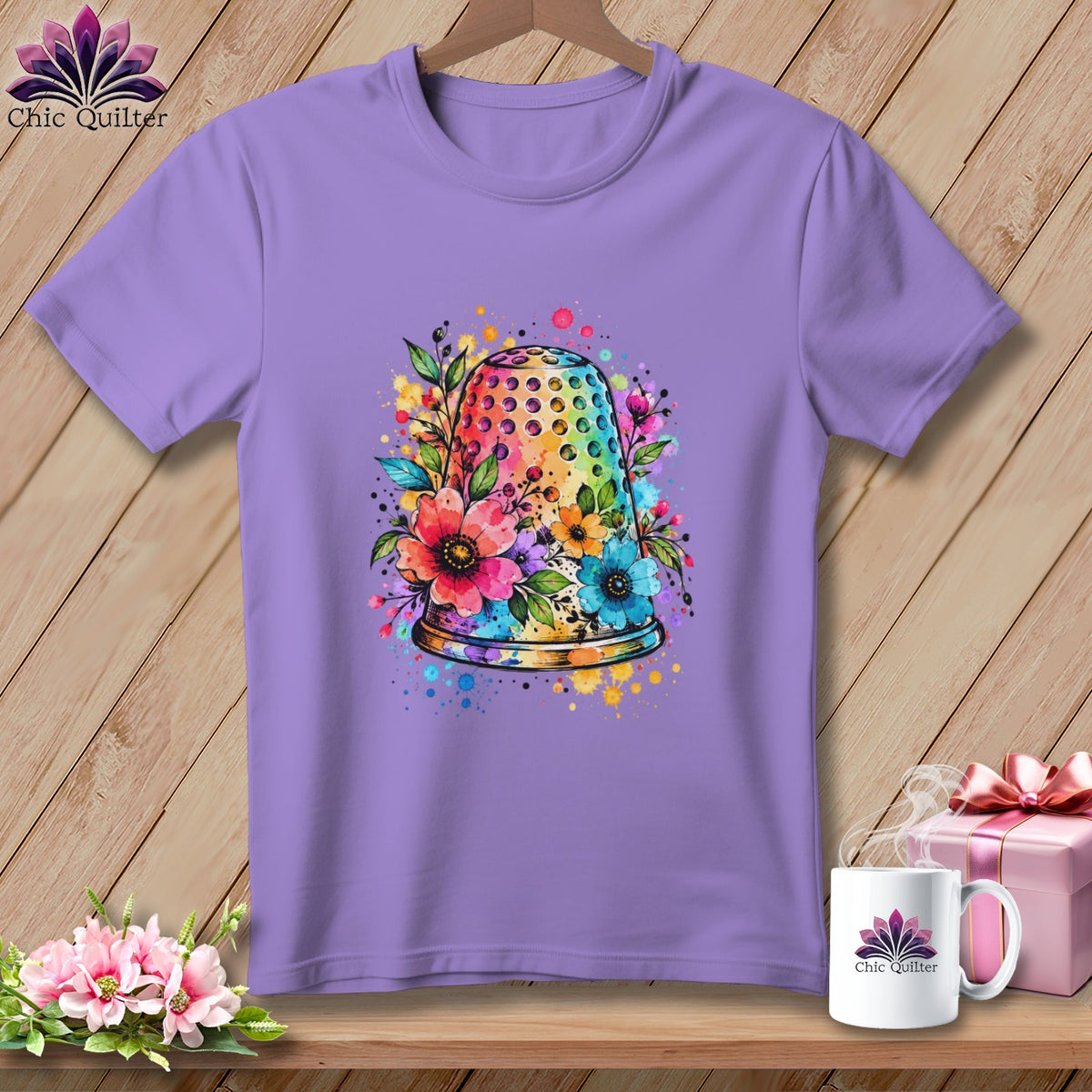 A purple t-shirt features a colorful watercolor thimble surrounded by flowers on a wooden background.