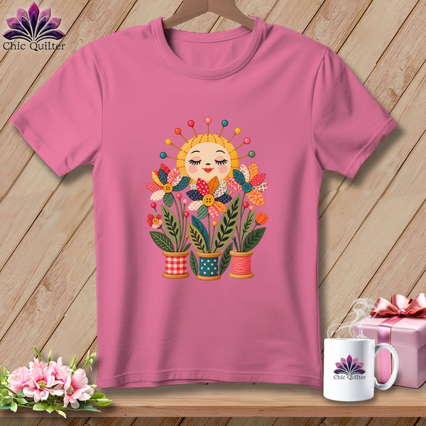 Pink t-shirt featuring a smiling sun head with pin rays and patchwork flowers in spool pots.