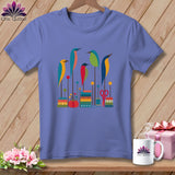 Periwinkle short-sleeve t-shirt with a graphic of colorful stylized birds, stacked spools of thread, and sewing accessories.