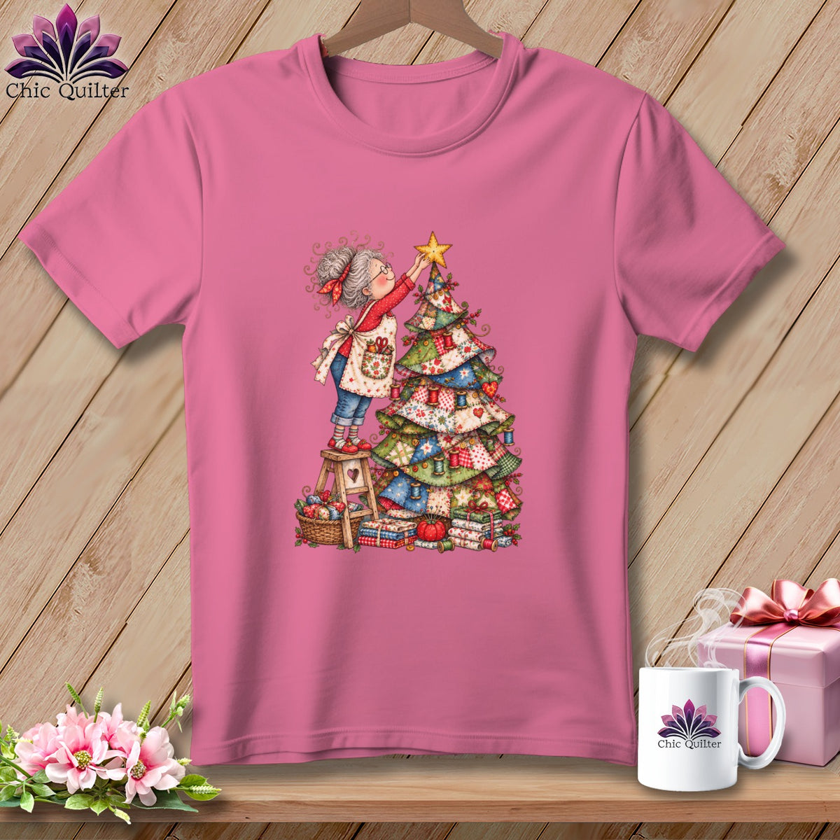 Pink t-shirt featuring a cartoon woman placing a star on a patchwork Christmas tree.