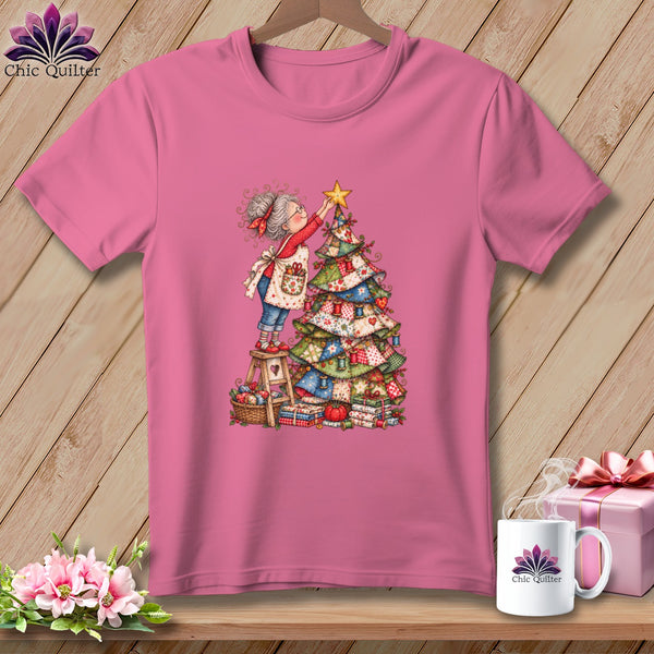 Pink t-shirt featuring a cartoon woman placing a star on a patchwork Christmas tree.