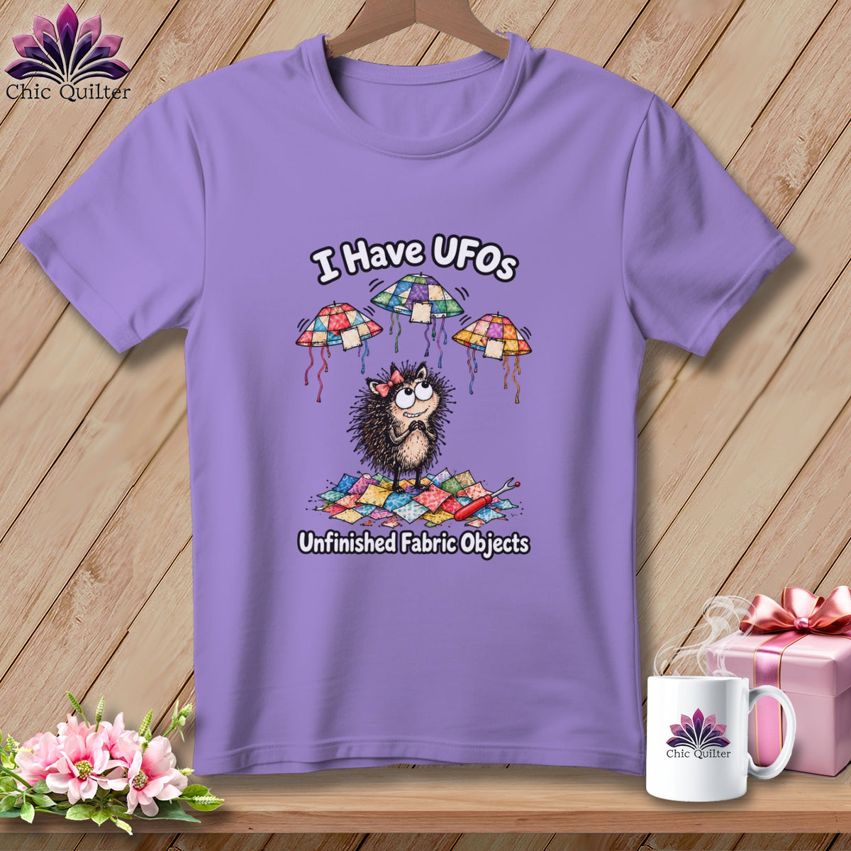 A purple t-shirt featuring a cartoon hedgehog with floating quilted UFOs and the text I Have UFOs Unfinished Fabric Objects.