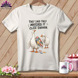White t-shirt featuring two geese, one with a patchwork wing, and text.