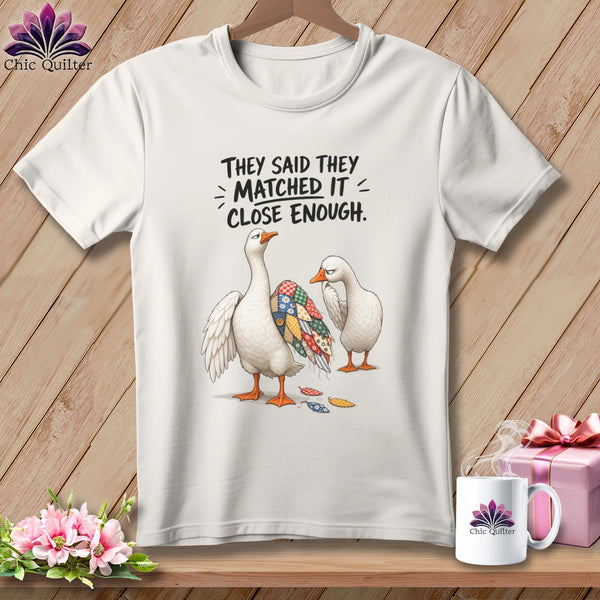 White t-shirt featuring two geese, one with a patchwork wing, and text.