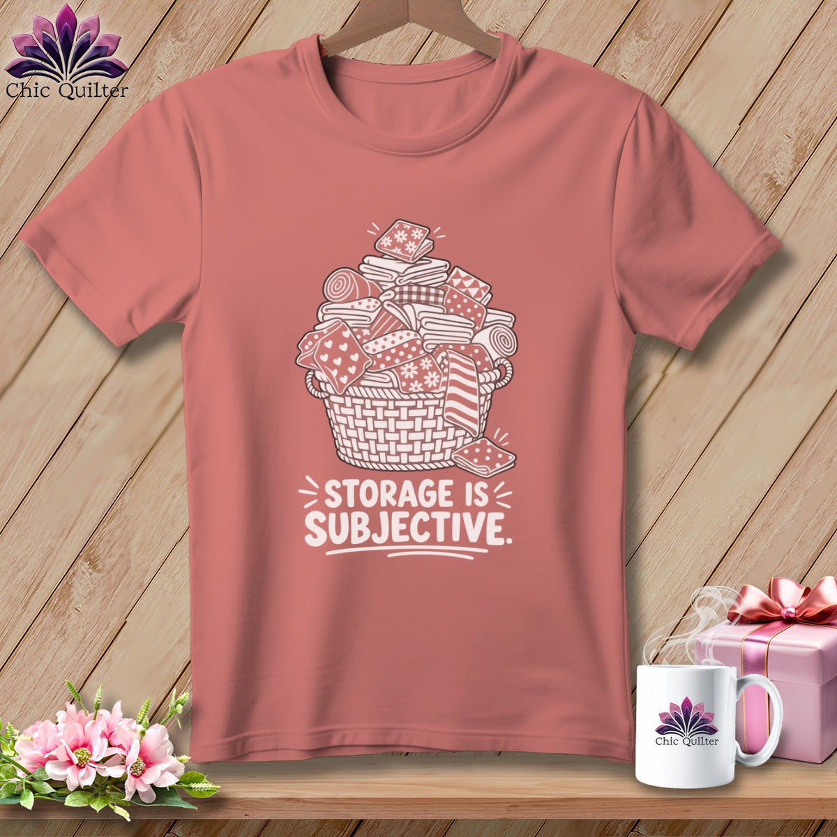Pink t-shirt with a graphic of a basket overflowing with fabric rolls and stacks, text reads "STORAGE IS SUBJECTIVE."