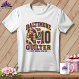 White t-shirt hanging on a wooden wall featuring Baltimore Quilter and number 10 graphics.