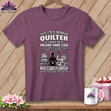 Mauve t-shirt hanging on a wooden background, featuring humorous quilting text and graphic art.