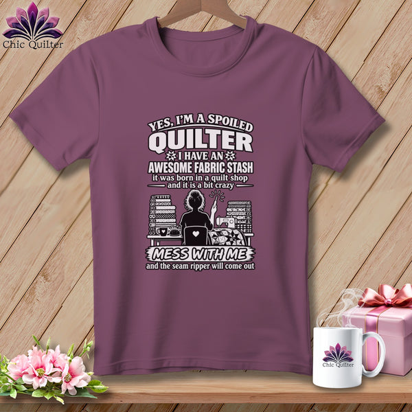 Mauve t-shirt hanging on a wooden background, featuring humorous quilting text and graphic art.