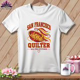 White crewneck t-shirt featuring a San Francisco Quilter graphic with buttons, ribbons, and text on a wooden background.