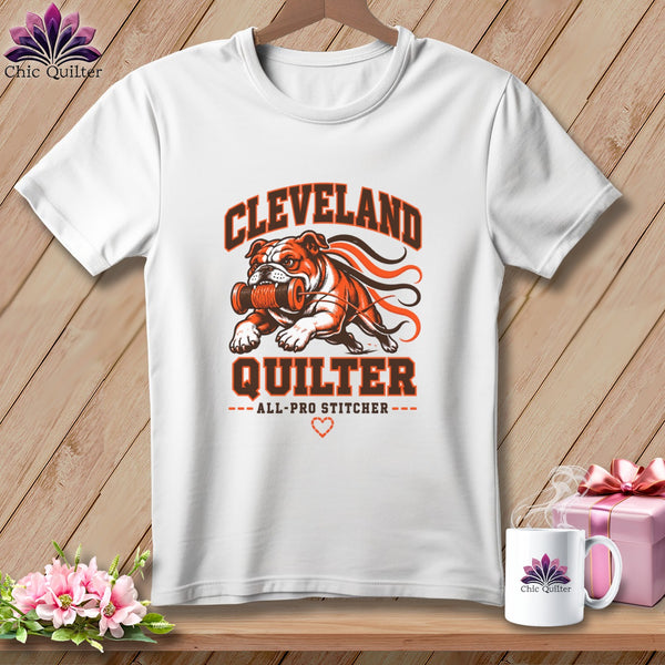 White crewneck t-shirt with orange and black graphic featuring a bulldog carrying a spool and the text "Cleveland Quilter".