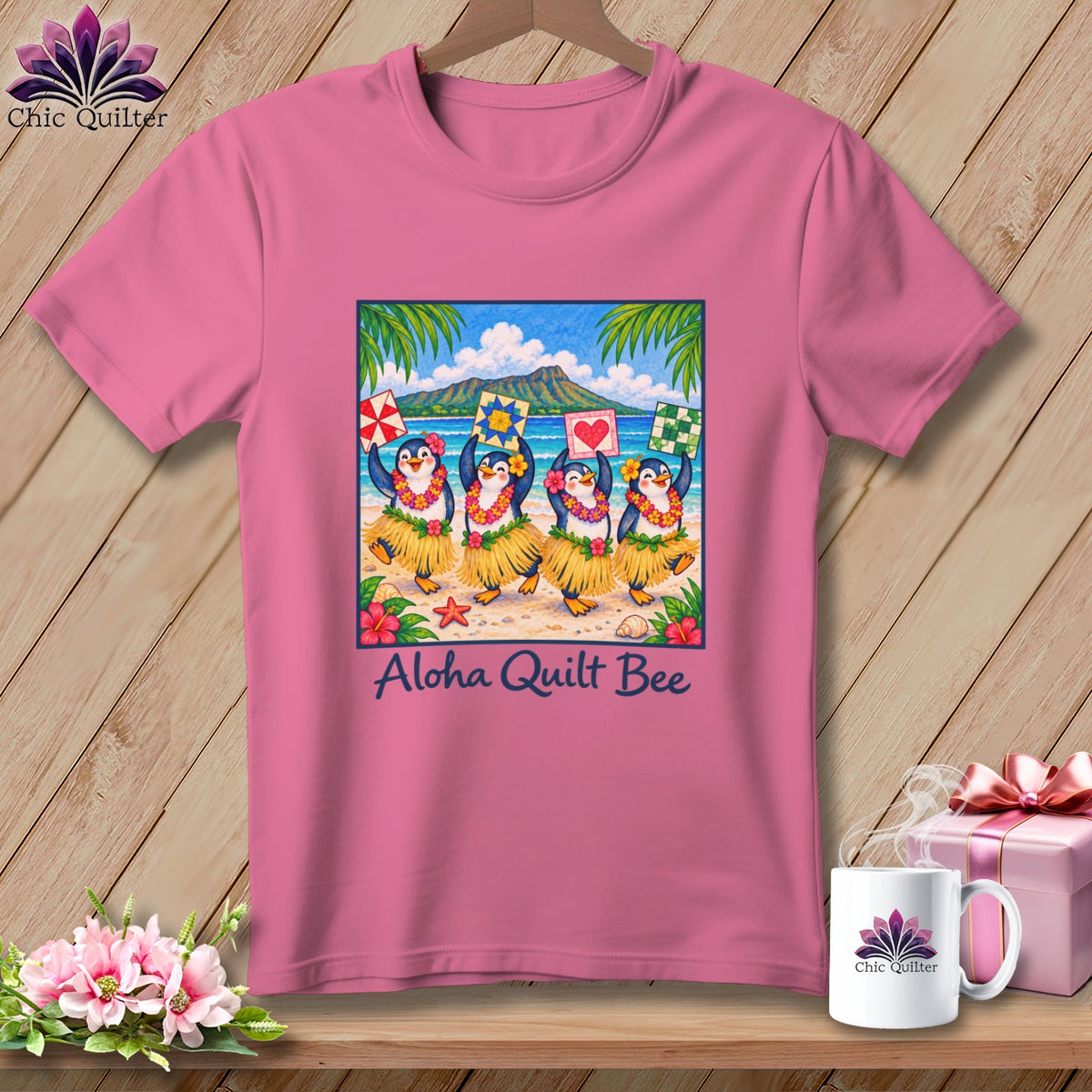 Pink t-shirt with a graphic of four hula-dancing penguins on a beach, text reading Aloha Quilt Bee.