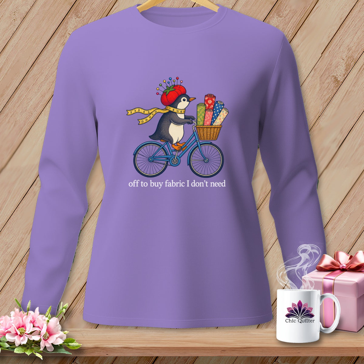 Penguin on a bicycle with fabric rolls, wearing a tomato pincushion hat, text "off to buy fabric I don't need".