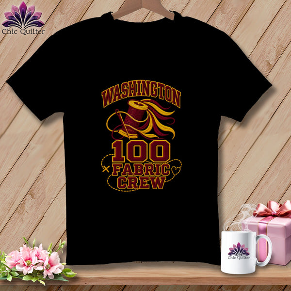 A black t-shirt hanging on a wooden wall features a graphic with a spool of thread and the text "Washington 100 Fabric Crew."