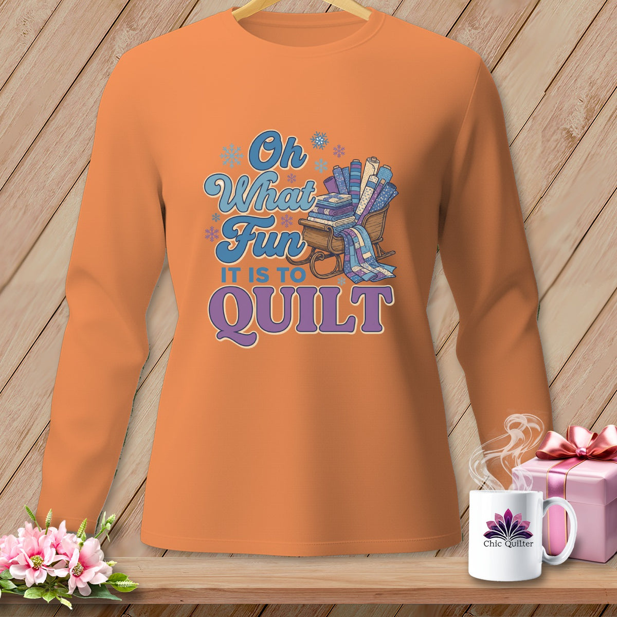 Orange long-sleeve shirt with "Oh What Fun It Is To Quilt" text and sleigh of fabric rolls.