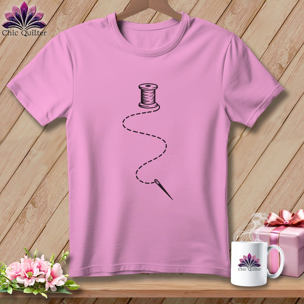 Pink t-shirt with a black spool of thread and needle graphic.
