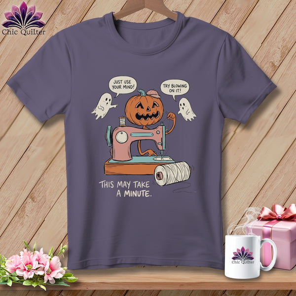 T-shirt with cartoon pumpkin at sewing machine, ghosts, and text "THIS MAY TAKE A MINUTE."
