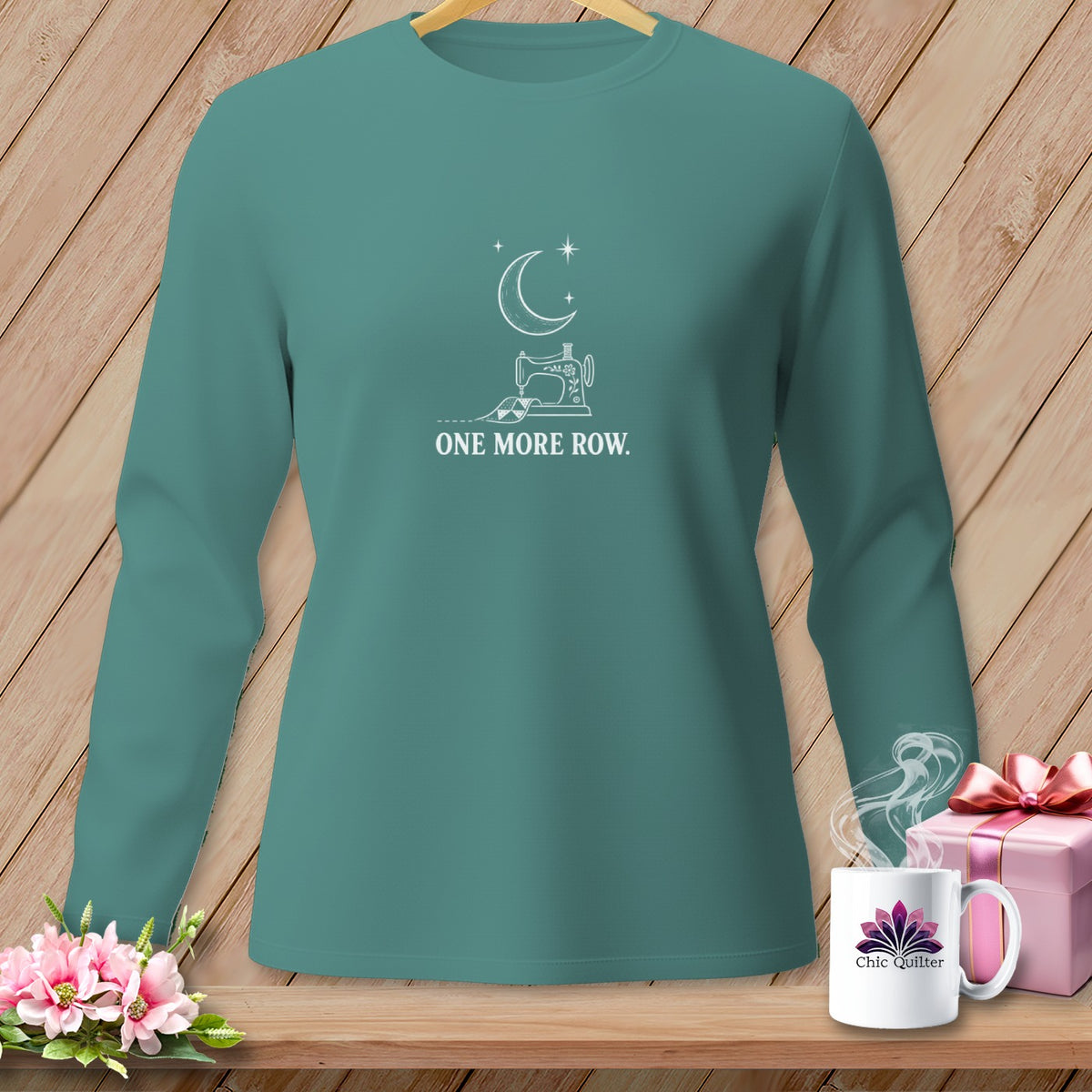 Teal long-sleeve shirt with white sewing machine, moon, stars, and "ONE MORE ROW." text.