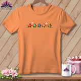 An orange crewneck t-shirt featuring a cartoon graphic of five colorful, running thimbles against a wooden background.