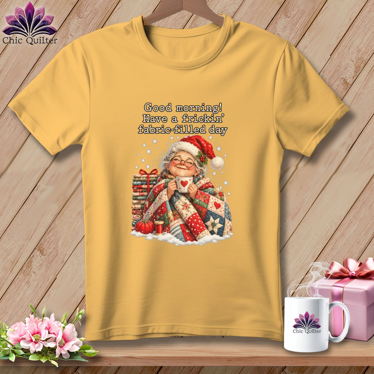 A mustard yellow t-shirt with a graphic of an elderly woman holding a mug, wrapped in a quilt, and text reading "Good morning! Have a frickin' fabric-filled day."