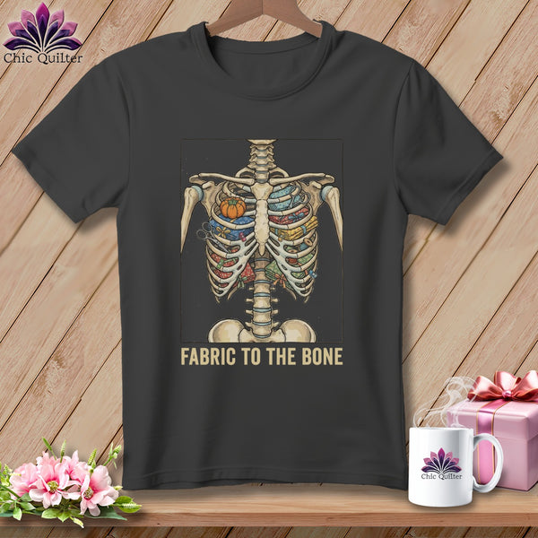 Dark gray t-shirt with a skeleton ribcage filled with fabric and sewing items. Text reads "FABRIC TO THE BONE".
