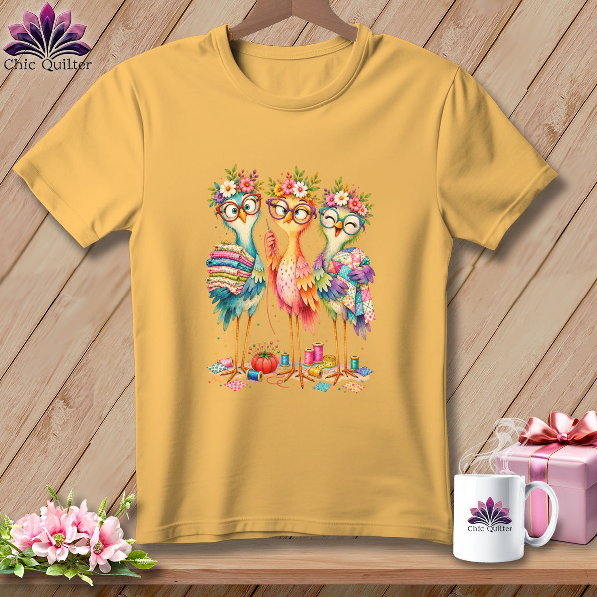 Gold t-shirt featuring an illustration of three colorful birds sewing and quilting, surrounded by sewing supplies.