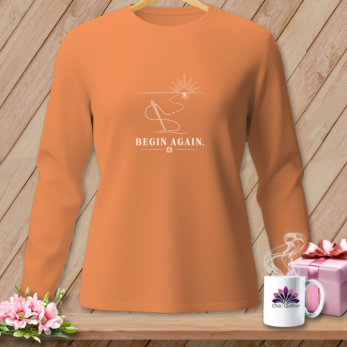 Orange long sleeve shirt with a white line art graphic of a needle, thread, and sunrise.