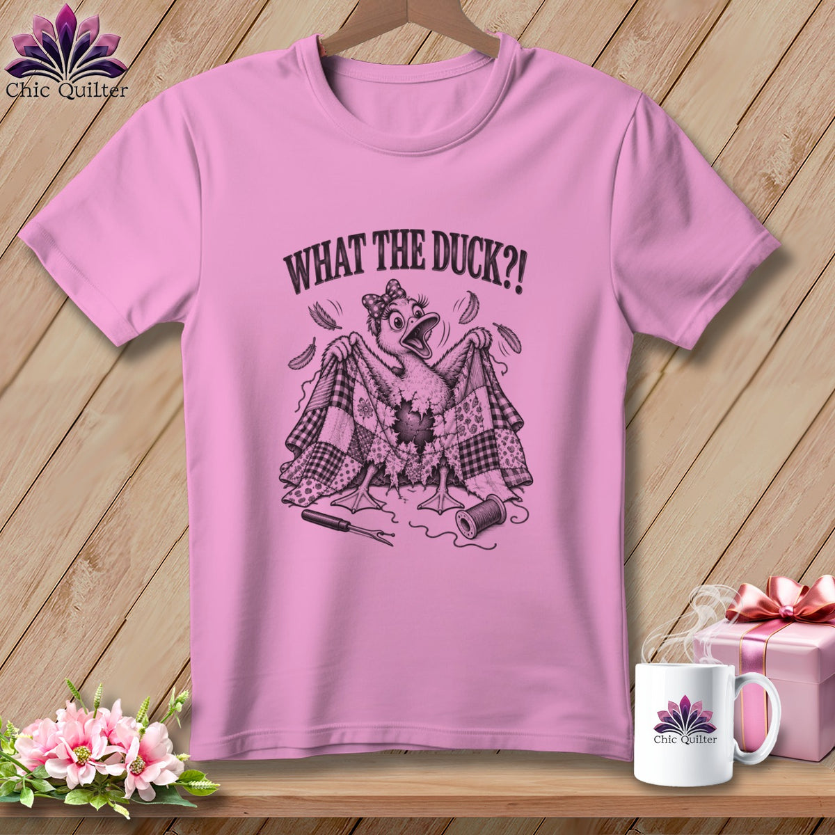 A pink t-shirt with a cartoon duck holding a torn quilt, featuring the text "WHAT THE DUCK?!".