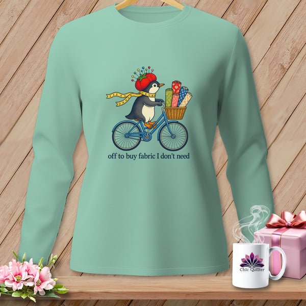 Penguin on a bicycle with fabric rolls and text "off to buy fabric I don't need".
