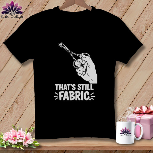 Black t-shirt with scissors cutting fabric, text "THAT'S STILL FABRIC".