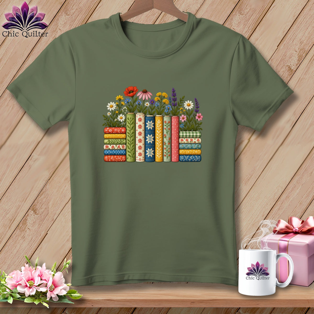 An olive green t-shirt features a colorful graphic of patterned books and wildflowers on a wooden surface.