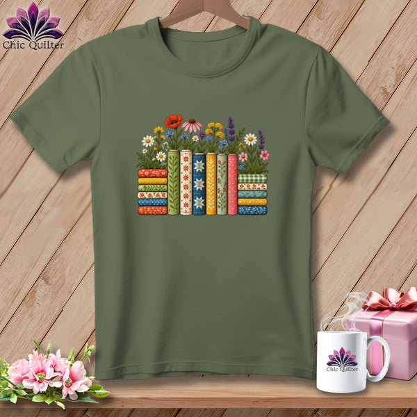 An olive green t-shirt features a colorful graphic of patterned books and wildflowers on a wooden surface.
