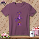 Plum-colored crewneck t-shirt featuring a whimsical purple bird standing on a spool of thread while holding a needle.