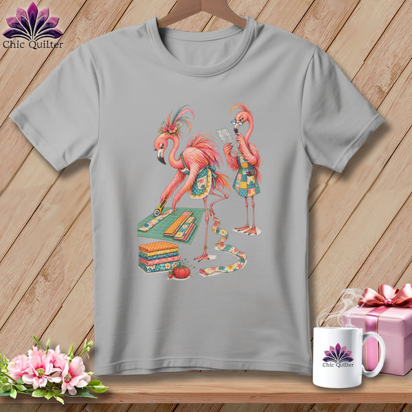 Two flamingos are shown quilting on a grey t-shirt.