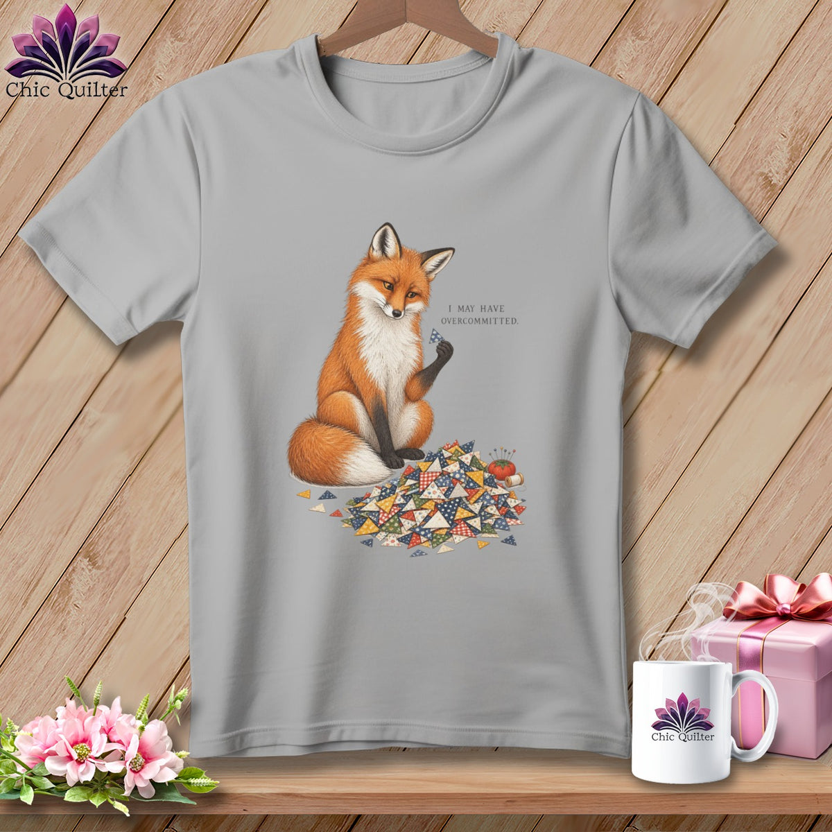 Grey t-shirt with a fox holding a quilt square and surrounded by fabric scraps.