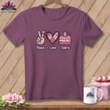 A purple t-shirt printed with a Peace Love Fabric design featuring a hand wearing a thimble, a quilted heart, and folded fabrics beneath a spool of thread.