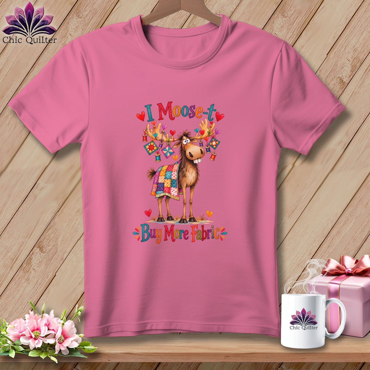 Pink t-shirt with a graphic of a moose wearing a quilt and the text I Moose-t Buy More Fabric.