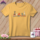 Yellow crewneck t-shirt featuring an illustration of five cats sitting on patterned cushions.