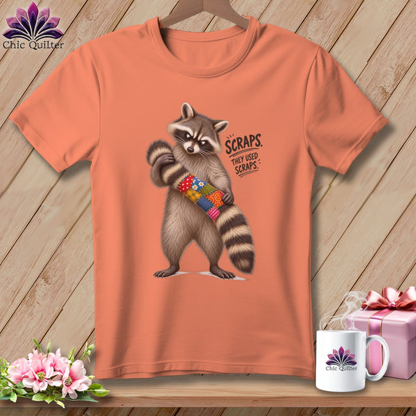 Peach t-shirt with raccoon holding patchwork tube, "SCRAPS" text.