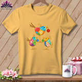 Gold short-sleeve t-shirt featuring a colorful patchwork design of three whimsical metal birds holding buttons.
