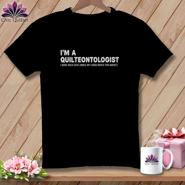 Black t-shirt with white text: "I'M A QUILTEONTOLOGIST I MAKE BOLD CUTS (WHILE MY CHEEKS BRACE FOR IMPACT)"