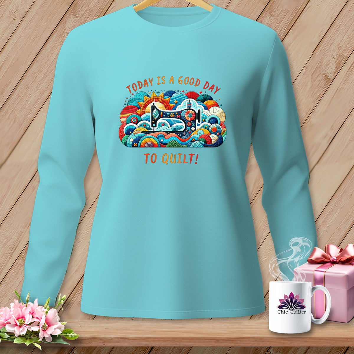 A light blue long-sleeved shirt featuring a graphic that says "TODAY IS A GOOD DAY TO QUILT!" with a sewing machine illustration.