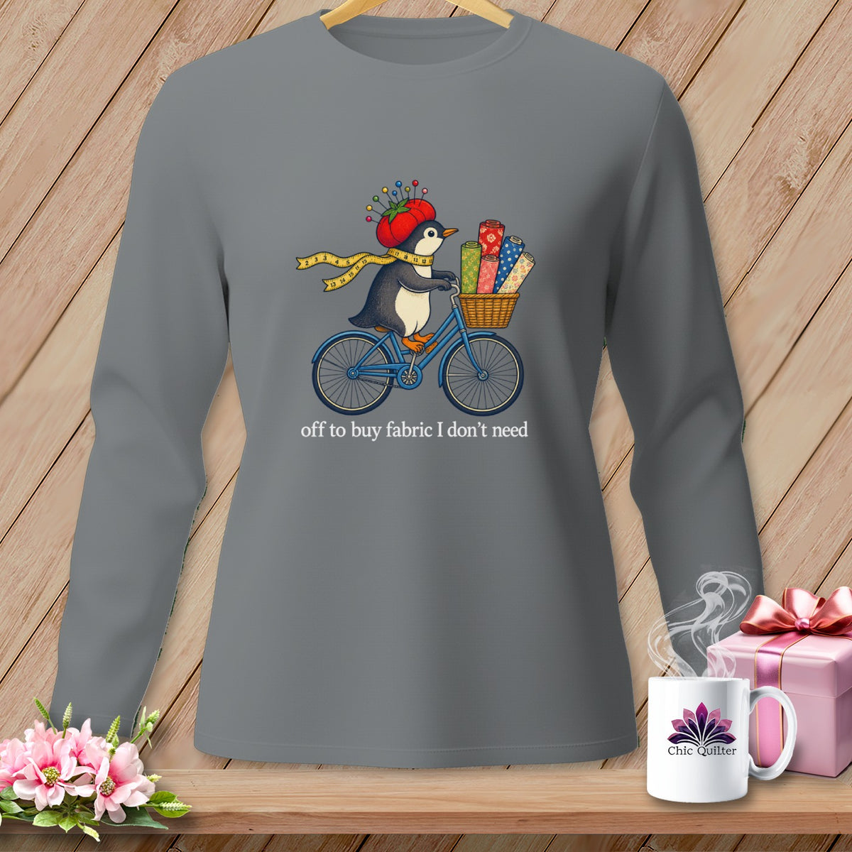 Penguin on bicycle with fabric rolls and sewing supplies, text reads "off to buy fabric I don't need".