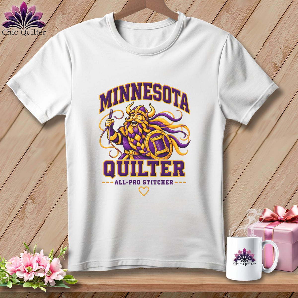 White t-shirt featuring a cartoon Viking holding a needle and shield, with Minnesota Quilter text.