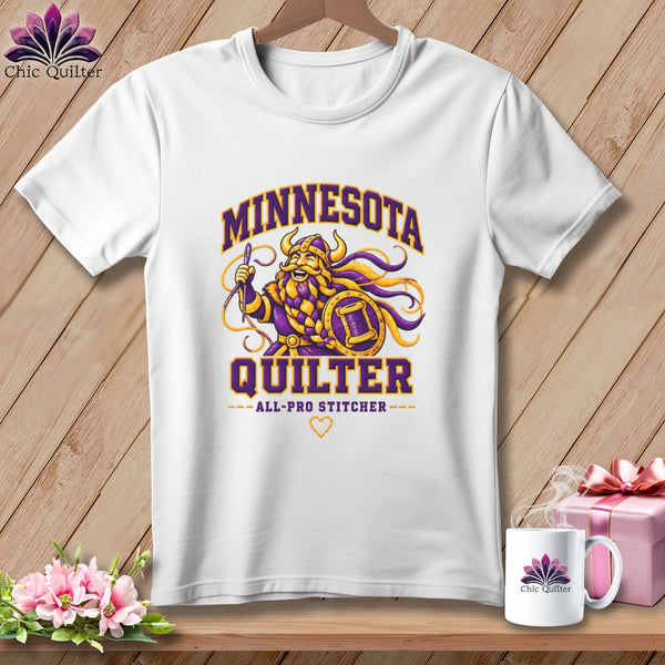 White t-shirt featuring a cartoon Viking holding a needle and shield, with Minnesota Quilter text.