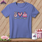 A periwinkle t-shirt features a graphic reading Peace Love Fabric, with a thimble, quilted heart, and folded fabrics.