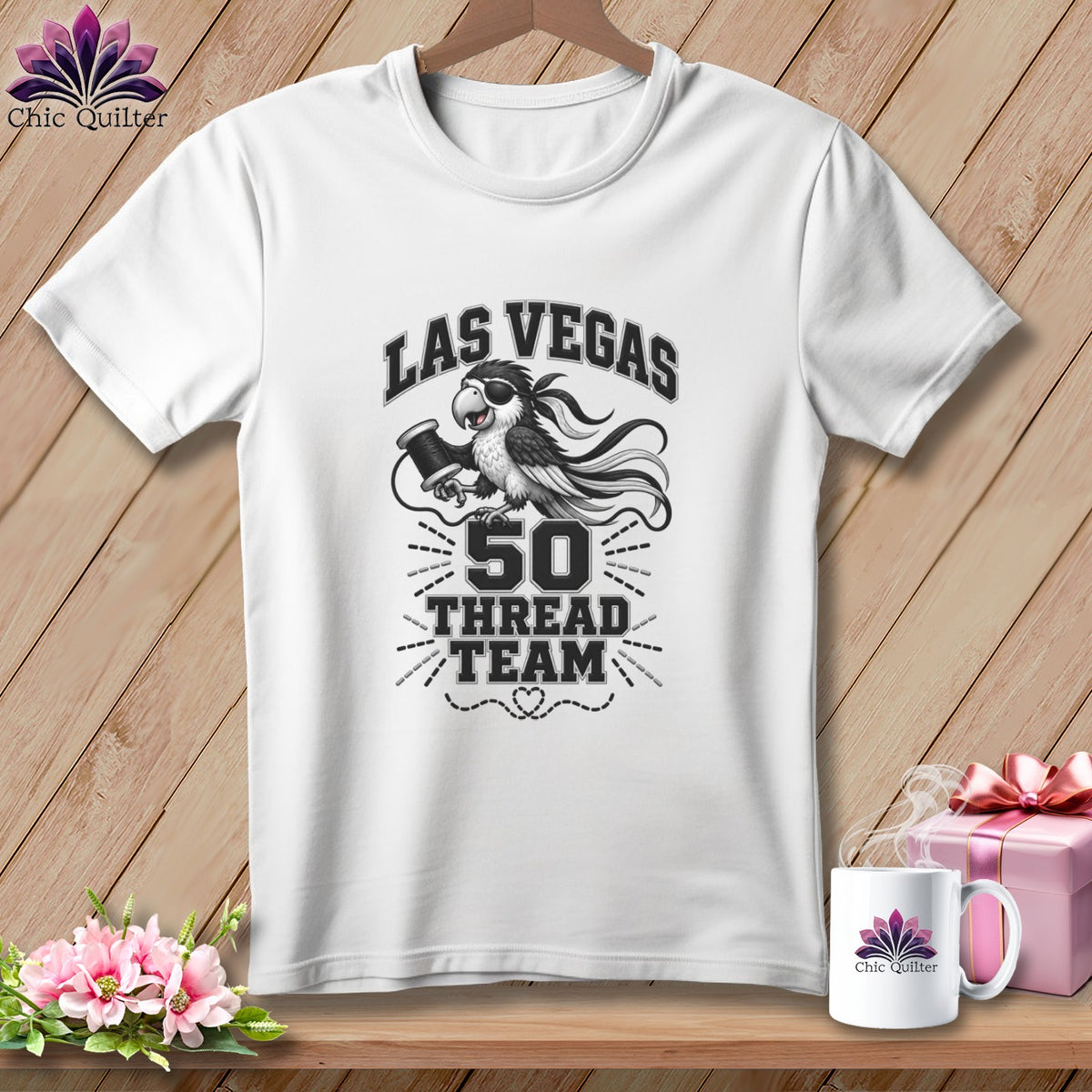 White t-shirt with a Las Vegas 50 Thread Team parrot graphic hanging on a wooden background.