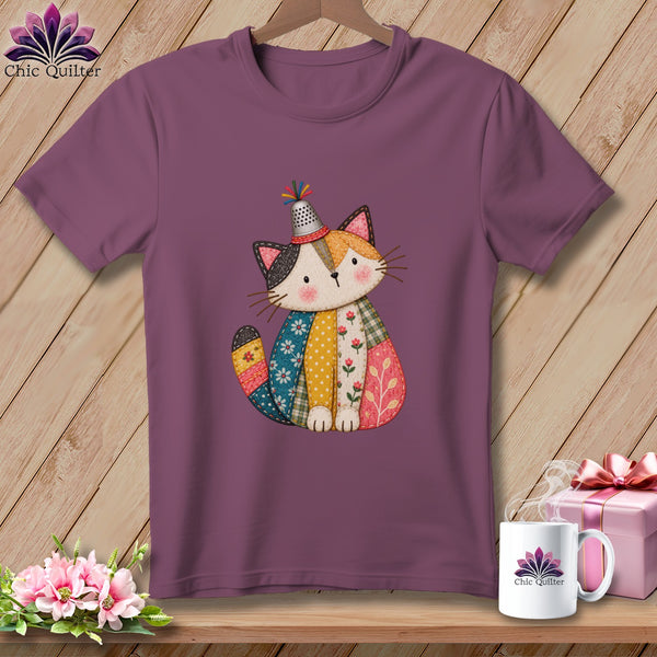 Purple t-shirt featuring a cute, quilted patchwork cat wearing a thimble hat, displayed on a wooden background.