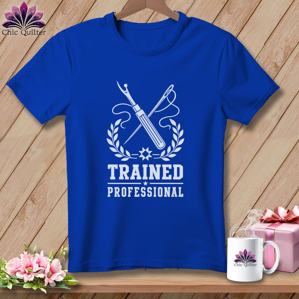 Blue t-shirt with white sewing tools, laurel wreath, and text "TRAINED PROFESSIONAL".
